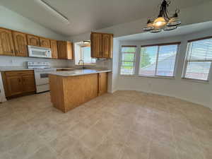 Kitchen area featuring wood cabinetry, white appliances, a center island with countertop seating, and tile flooring