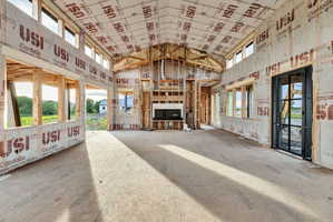Spacious unfinished room featuring a vaulted ceiling with exposed framing, an integrated fireplace unit, and a black-framed glass door