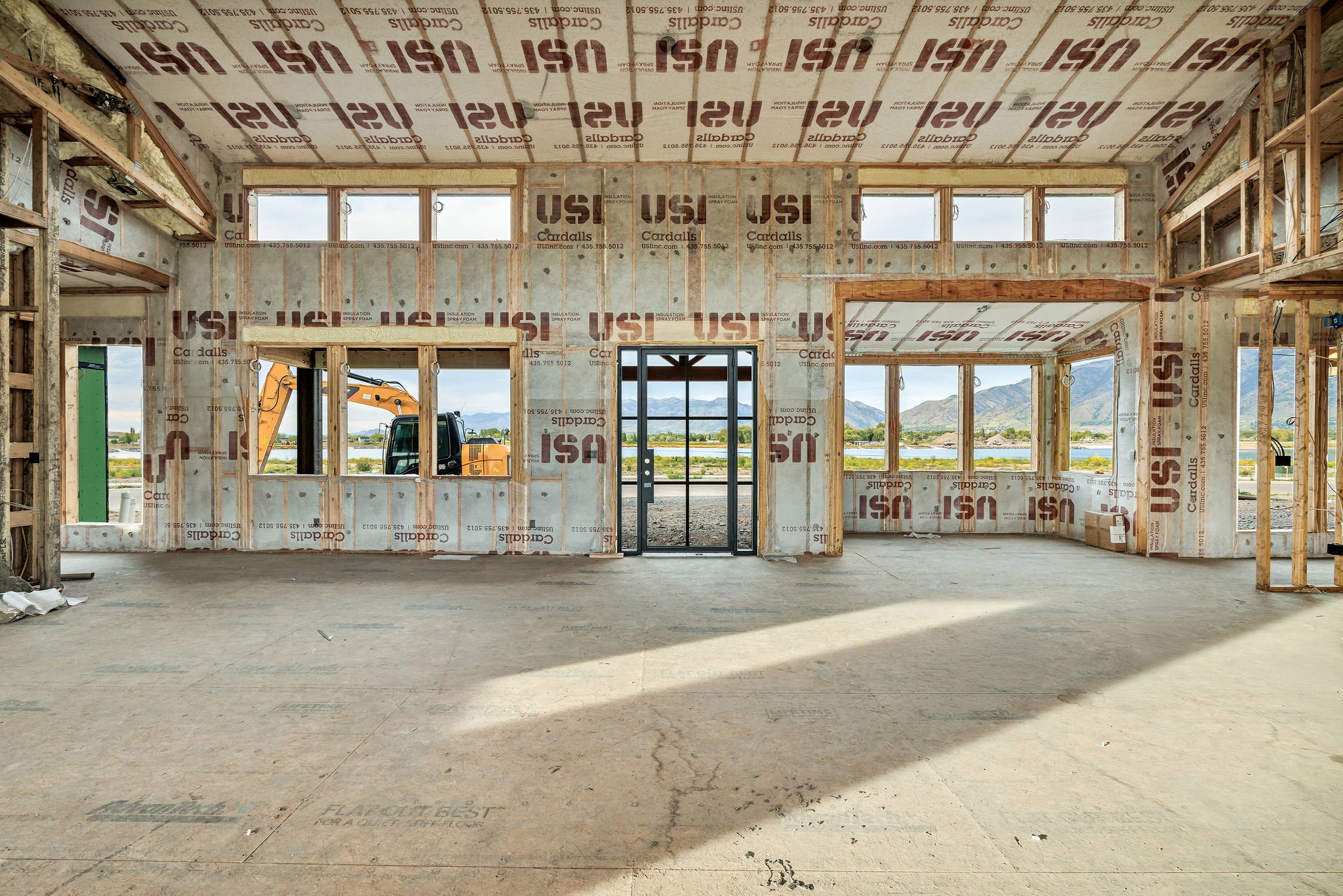 Expansive interior space under construction, featuring multiple large window openings, a framed door opening, and visible structural framing