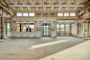 Expansive interior space under construction, featuring multiple large window openings, a framed door opening, and visible structural framing