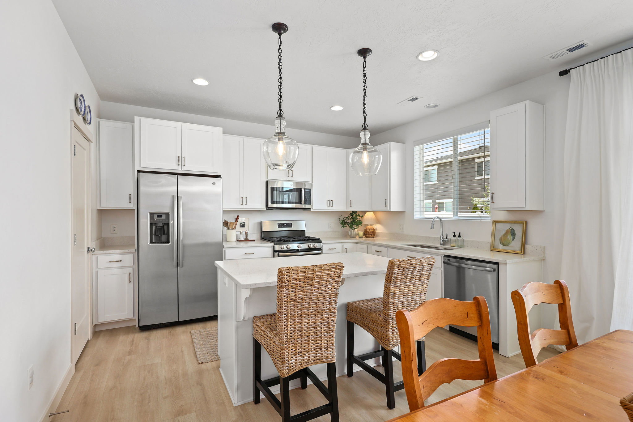 Bright kitchen featuring white cabinetry, stainless steel appliances, a center island with countertop seating, wood-finish flooring, and pendant lighting