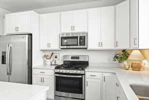 Bright kitchen featuring white shaker-style cabinetry, light-toned countertops, and stainless steel appliances including a refrigerator, range, and microwave