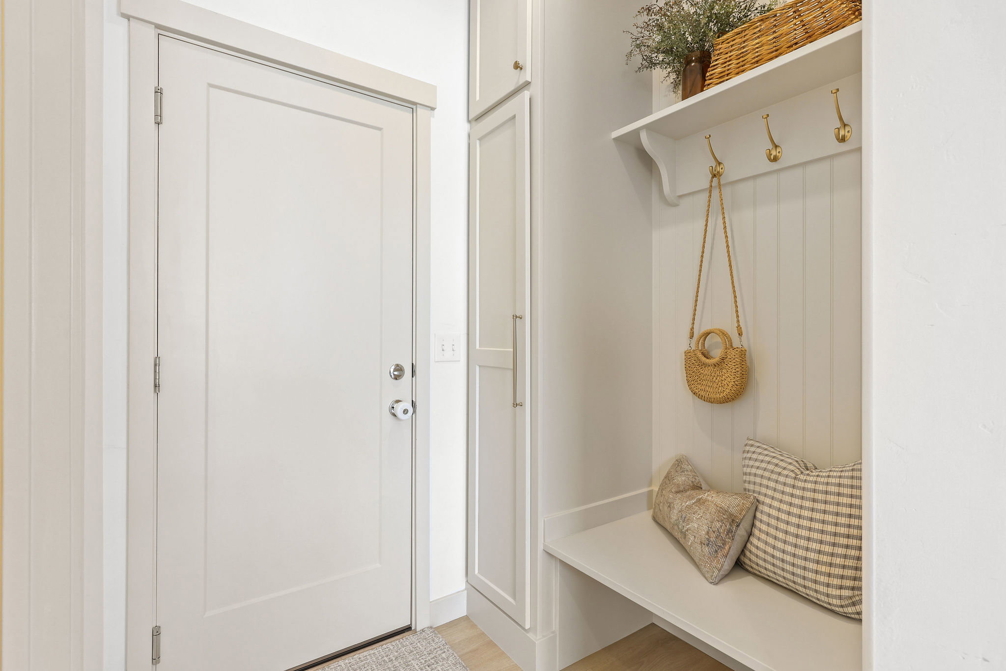 Entryway featuring a white paneled door, built-in storage cabinetry, a bench with beadboard backing, a white shelf, and brass-tone coat hooks