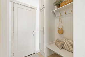 Entryway featuring a white paneled door, built-in storage cabinetry, a bench with beadboard backing, a white shelf, and brass-tone coat hooks