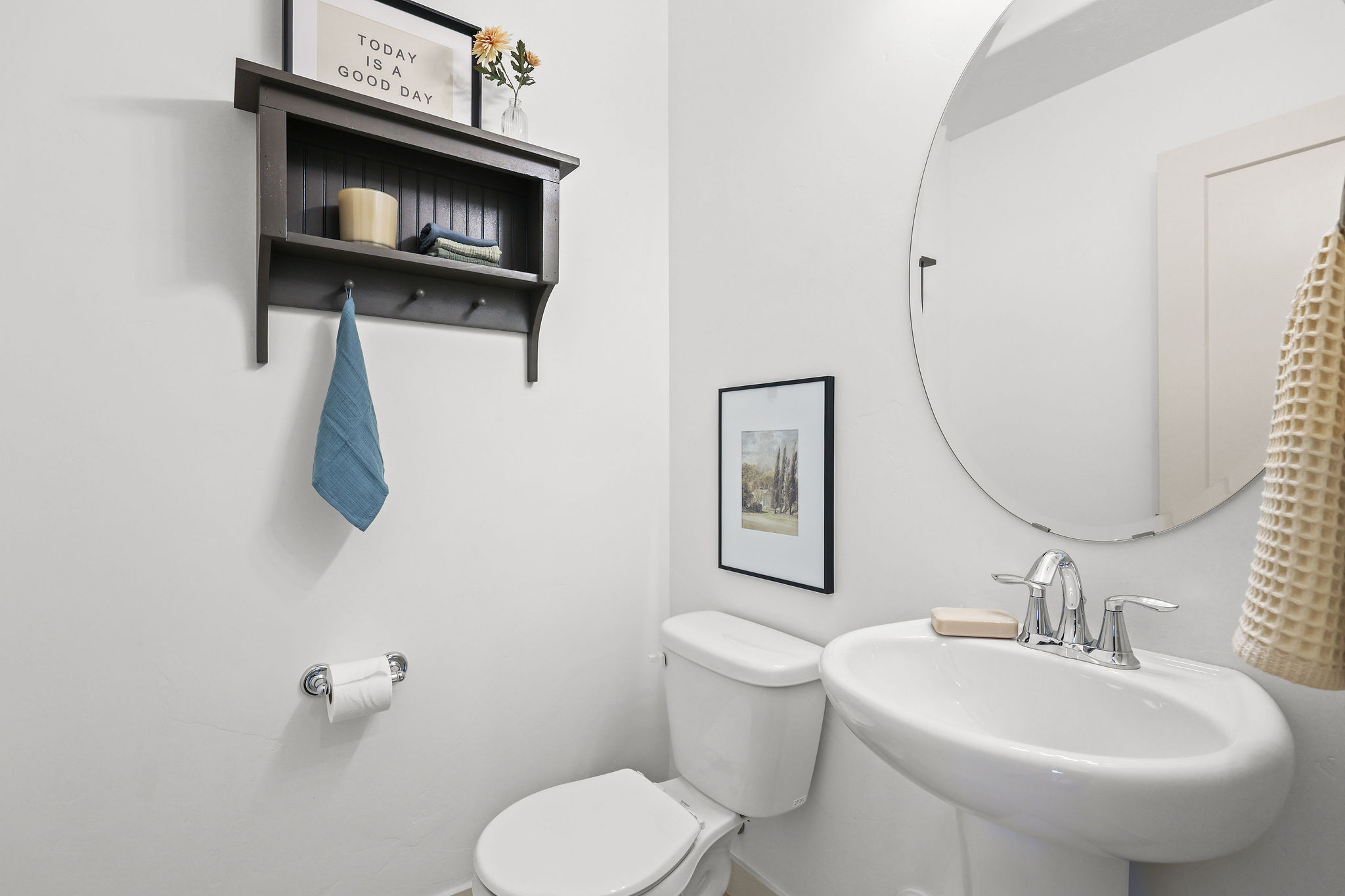 Pedestal sink with chrome fixtures and a circular frameless mirror