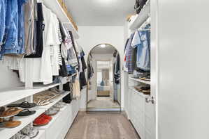 Walk-through closet featuring built-in shelving, hanging rods, integrated drawers, and carpet flooring