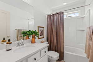 White vanity with a built-in sink and chrome faucet, large rectangular mirror, and an integrated white tub and shower combination with a transom window
