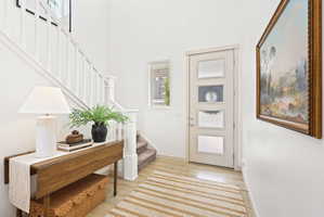 Entryway featuring light wood-finish flooring, a contemporary staircase with white balusters, and a modern door with frosted glass panels