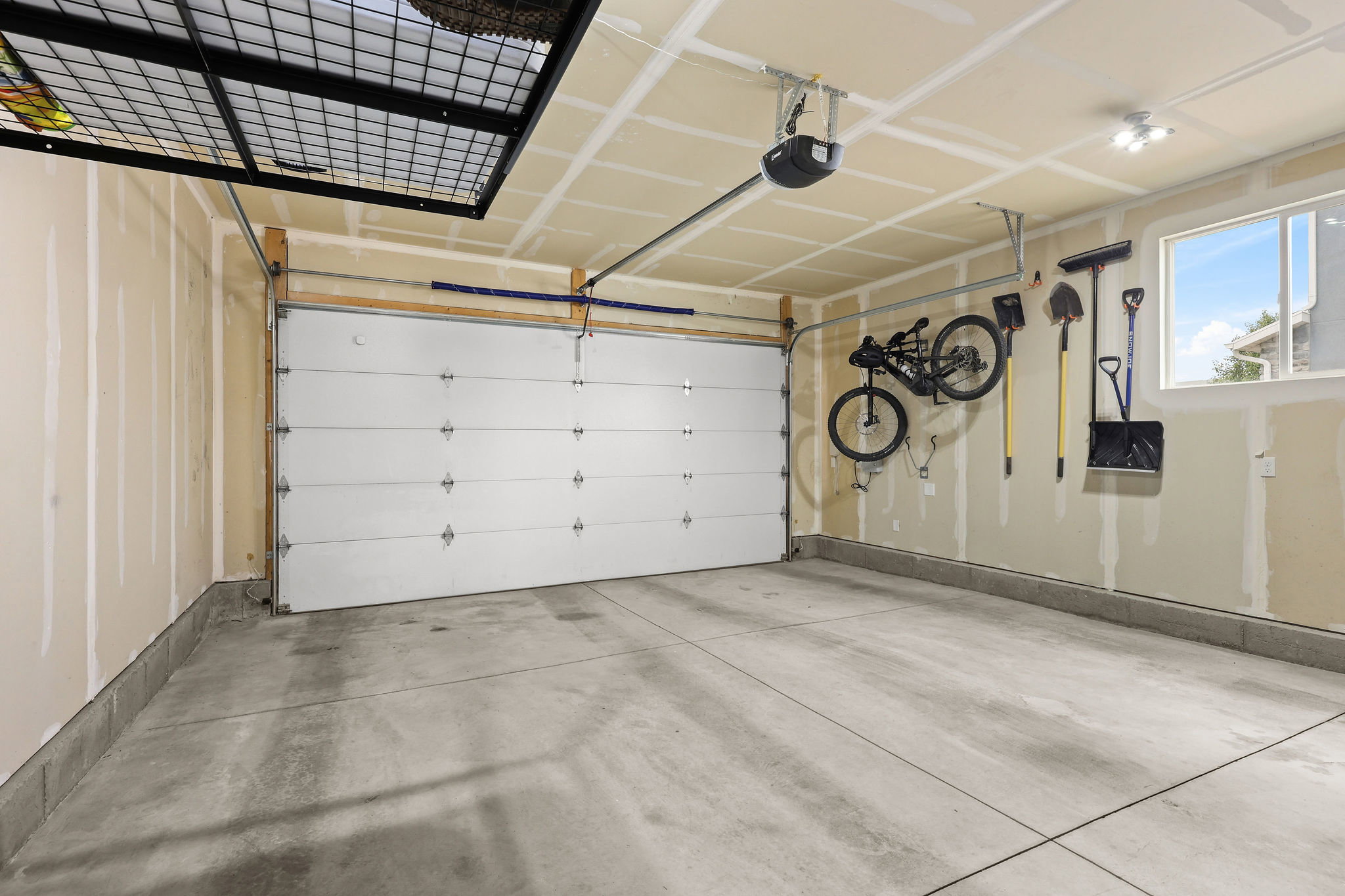 Concrete flooring garage with an overhead door, automatic opener, wall-mounted window, and track lighting