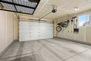 Concrete flooring garage with an overhead door, automatic opener, wall-mounted window, and track lighting