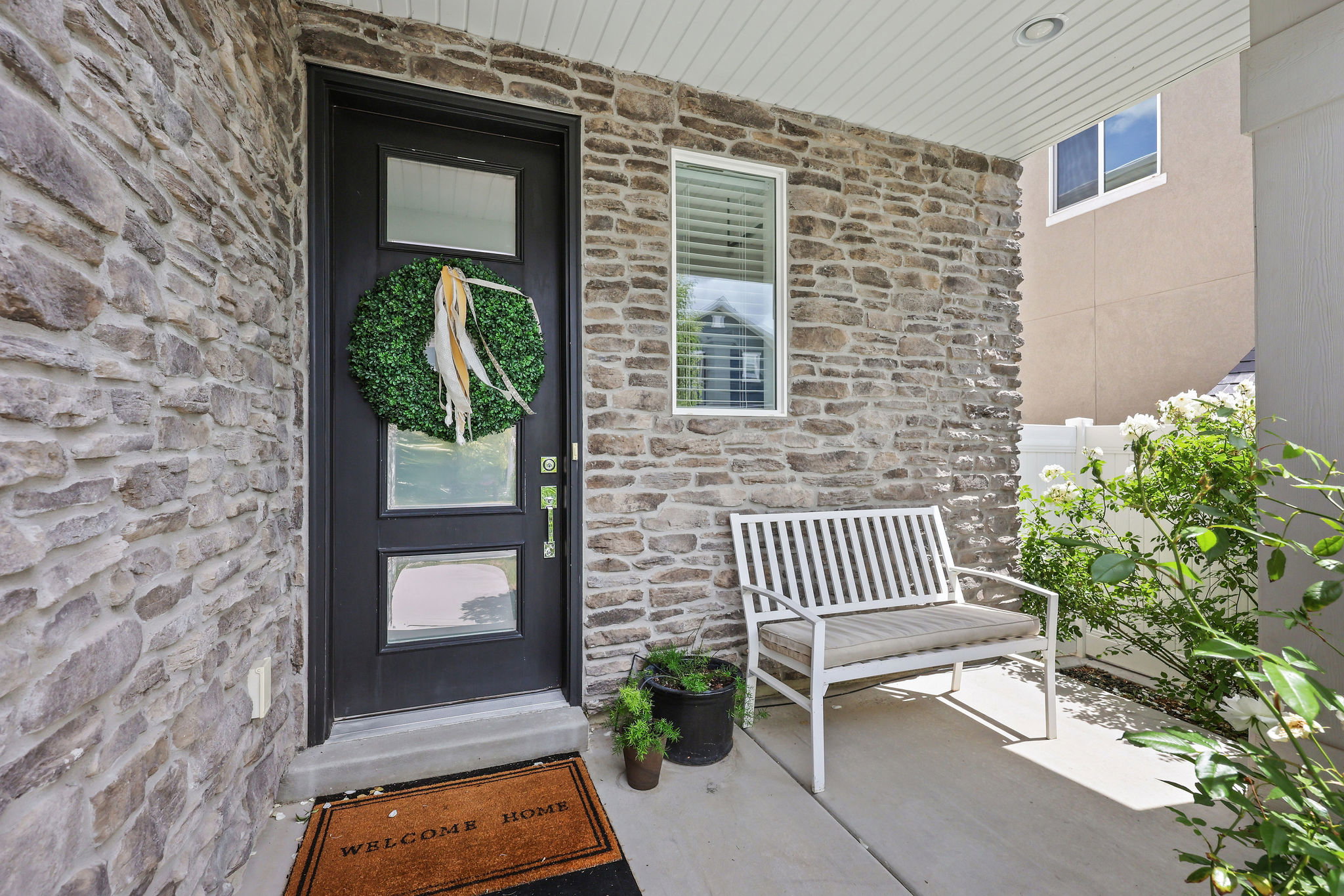 Stone veneer exterior featuring a black entry door with frosted glass panels, a concrete porch, and a white framed window