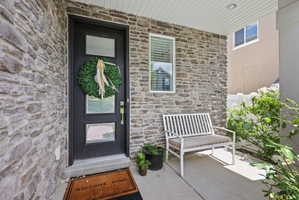 Stone veneer exterior featuring a black entry door with frosted glass panels, a concrete porch, and a white framed window