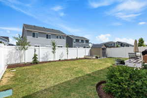 Expansive fenced backyard featuring a manicured lawn, established shrubbery, and a concrete patio area