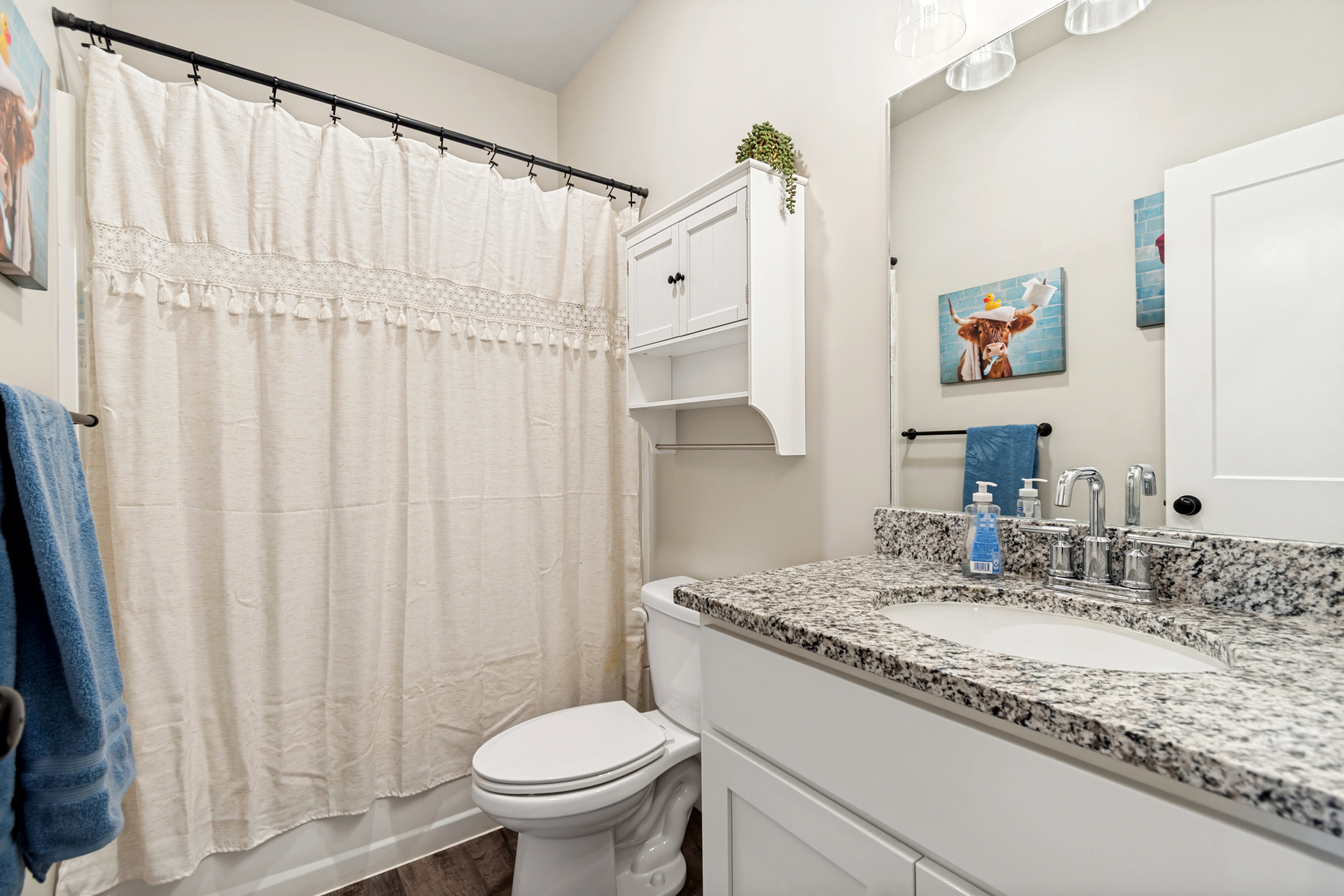 Bathroom featuring a shower with a decorative curtain, a white vanity cabinet, and a speckled countertop with an integrated sink