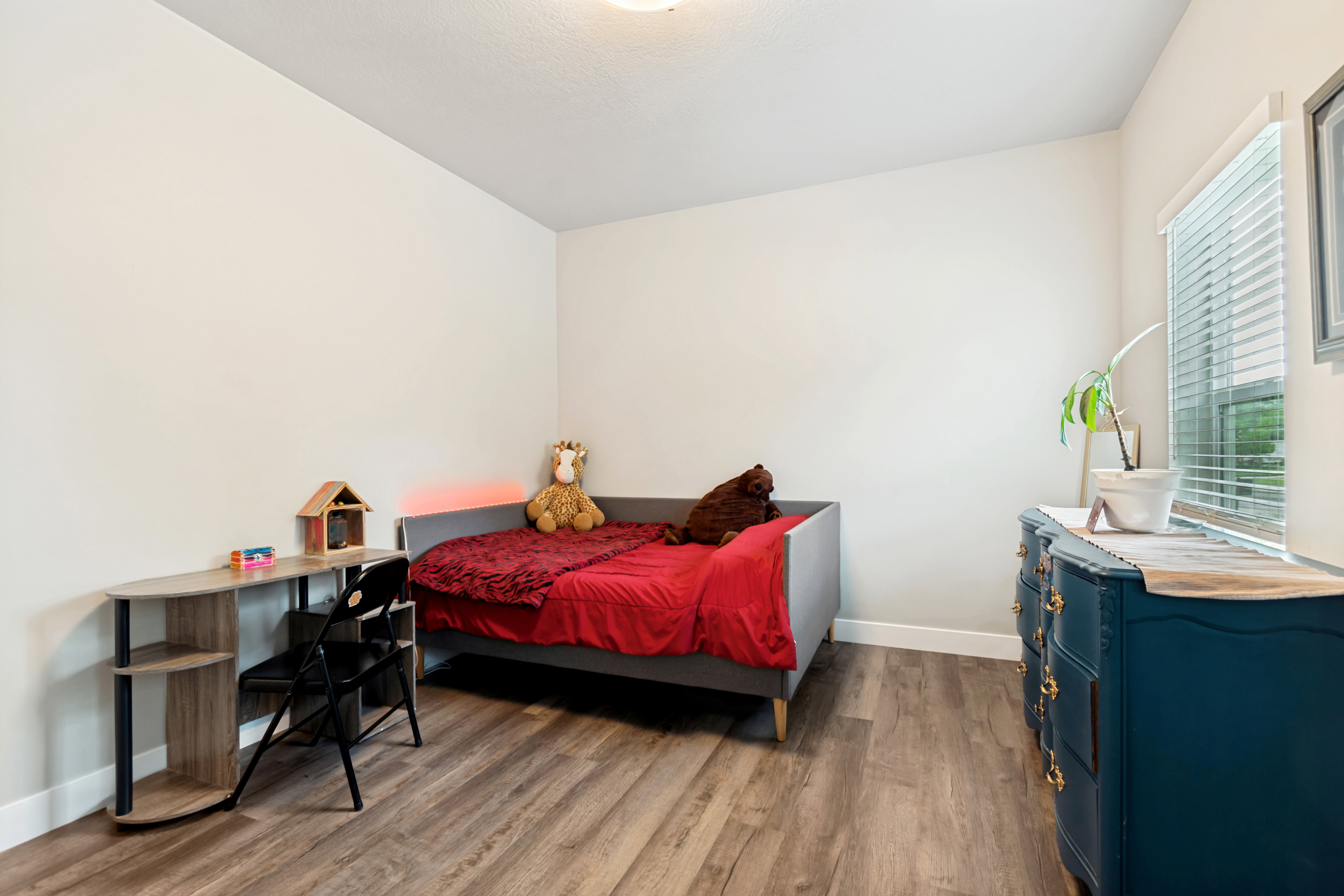 Neutral-toned room featuring wood-finish flooring, a bright window with horizontal blinds, and a flush-mount ceiling light