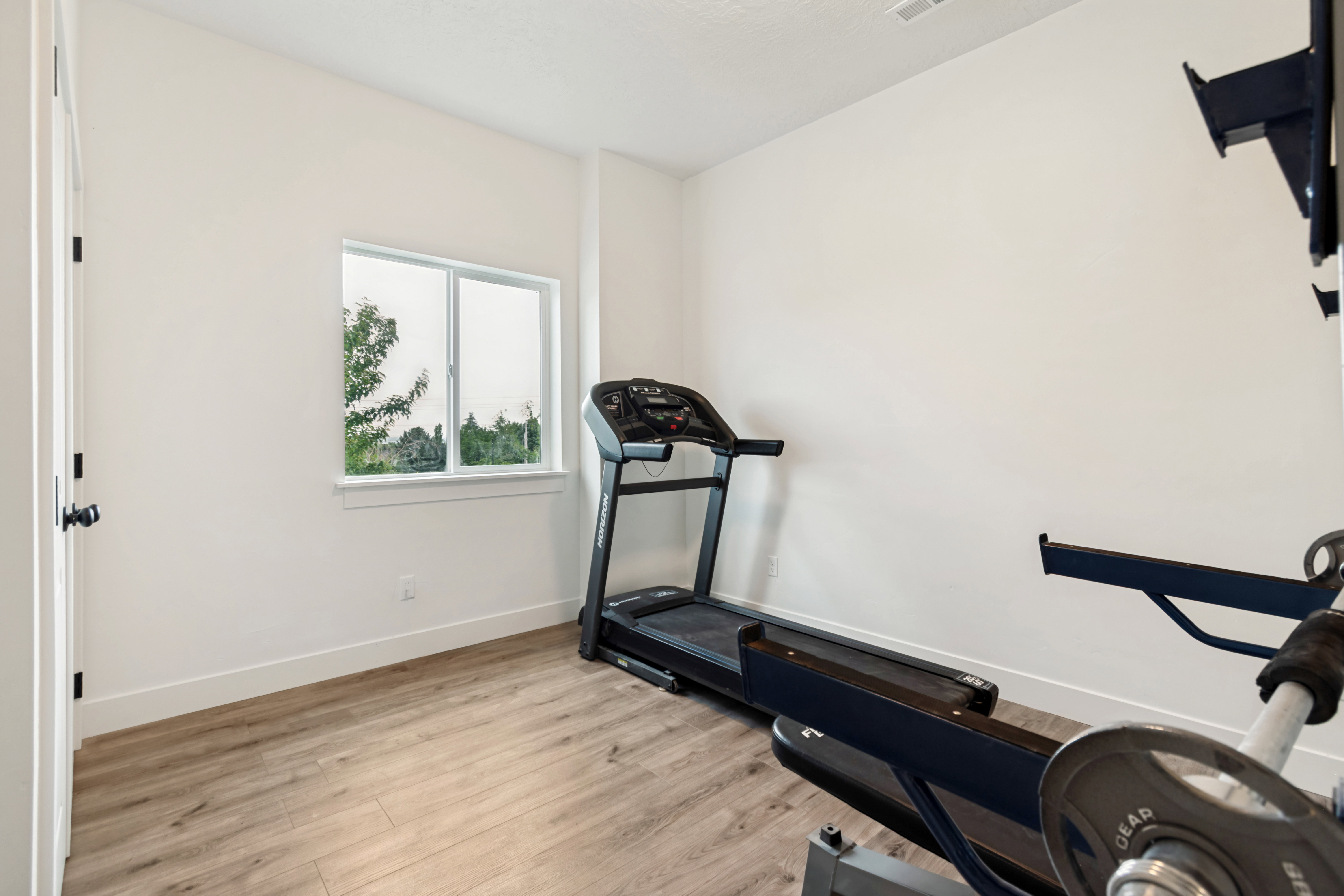 Room with wood-finish flooring, white walls, and a white trim baseboard