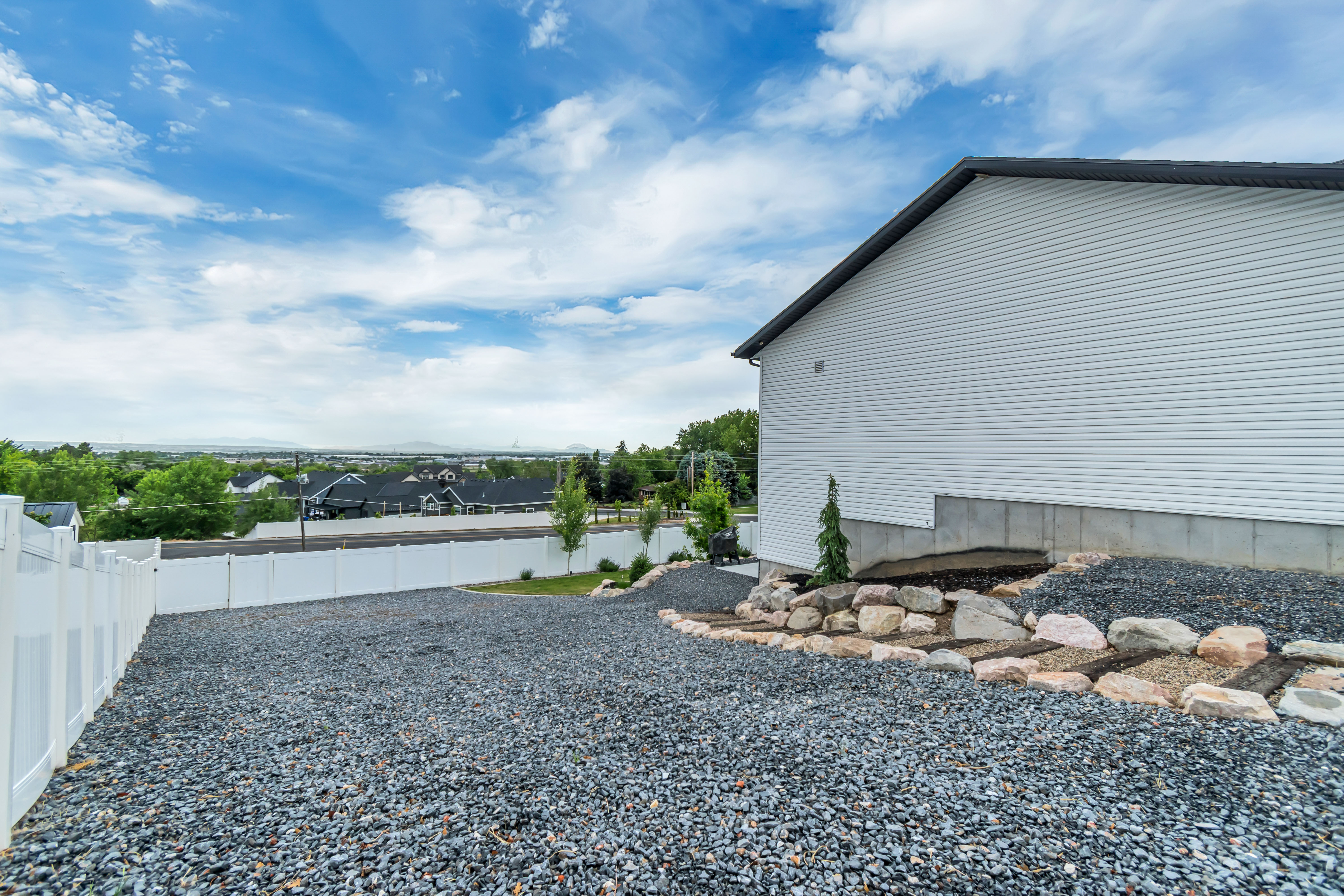 Gravel driveway with white vinyl fencing and a terraced rock landscape feature