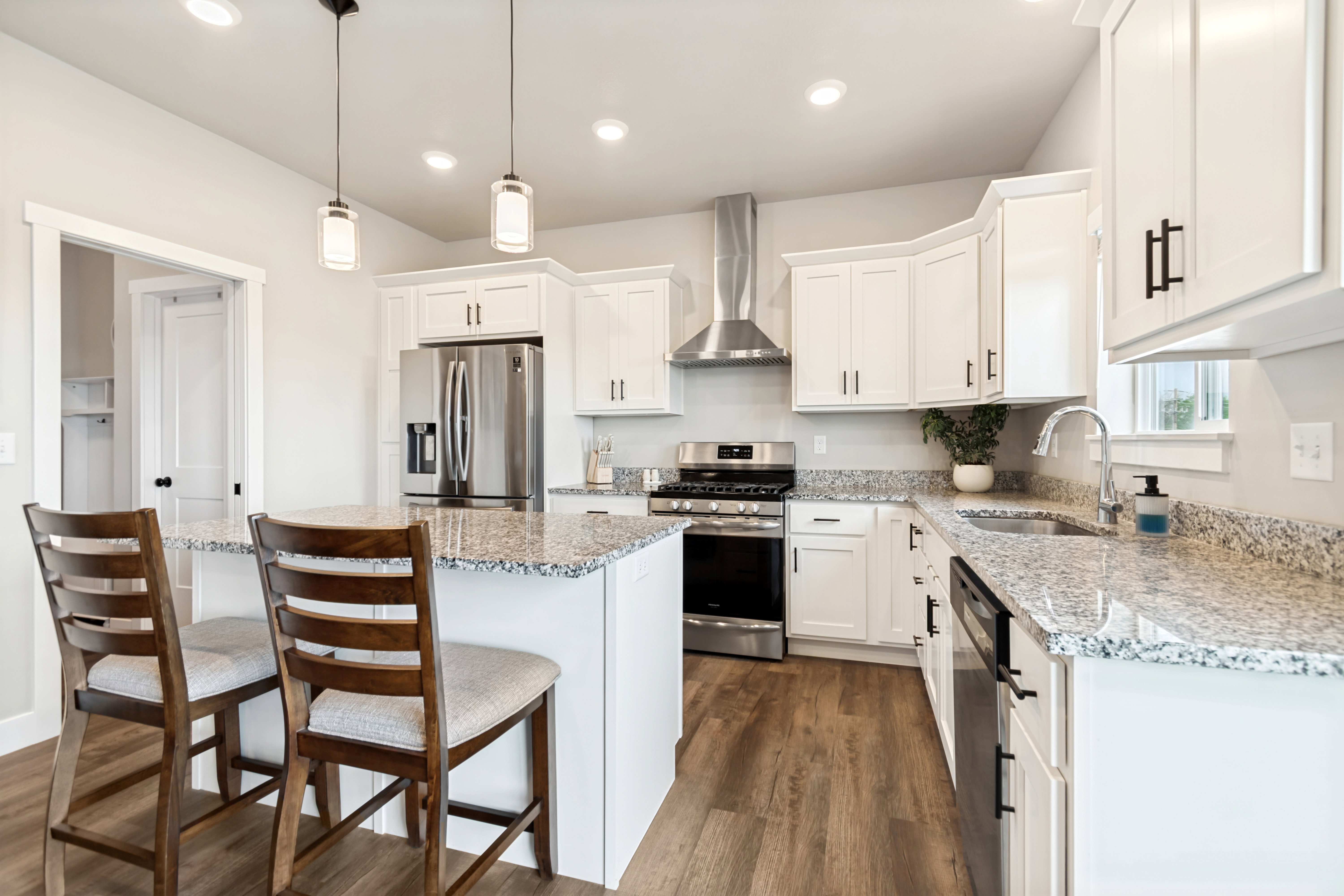 Kitchen featuring white cabinetry with black hardware, granite countertops, stainless steel appliances, wood-finish flooring, and recessed lighting