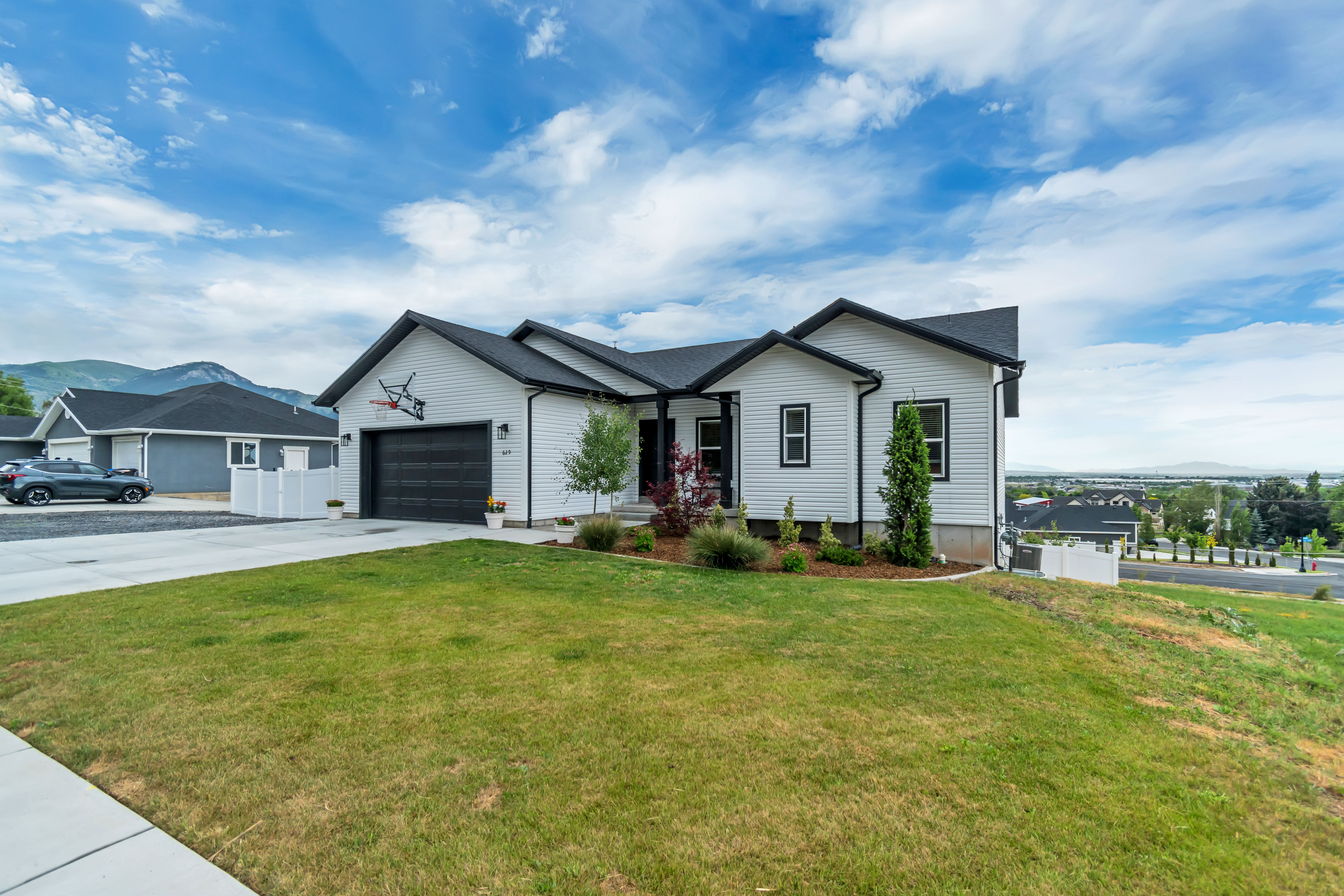 Contemporary exterior featuring white siding with black trim, a dark asphalt shingle roof, an attached garage with a black door, and a concrete driveway
