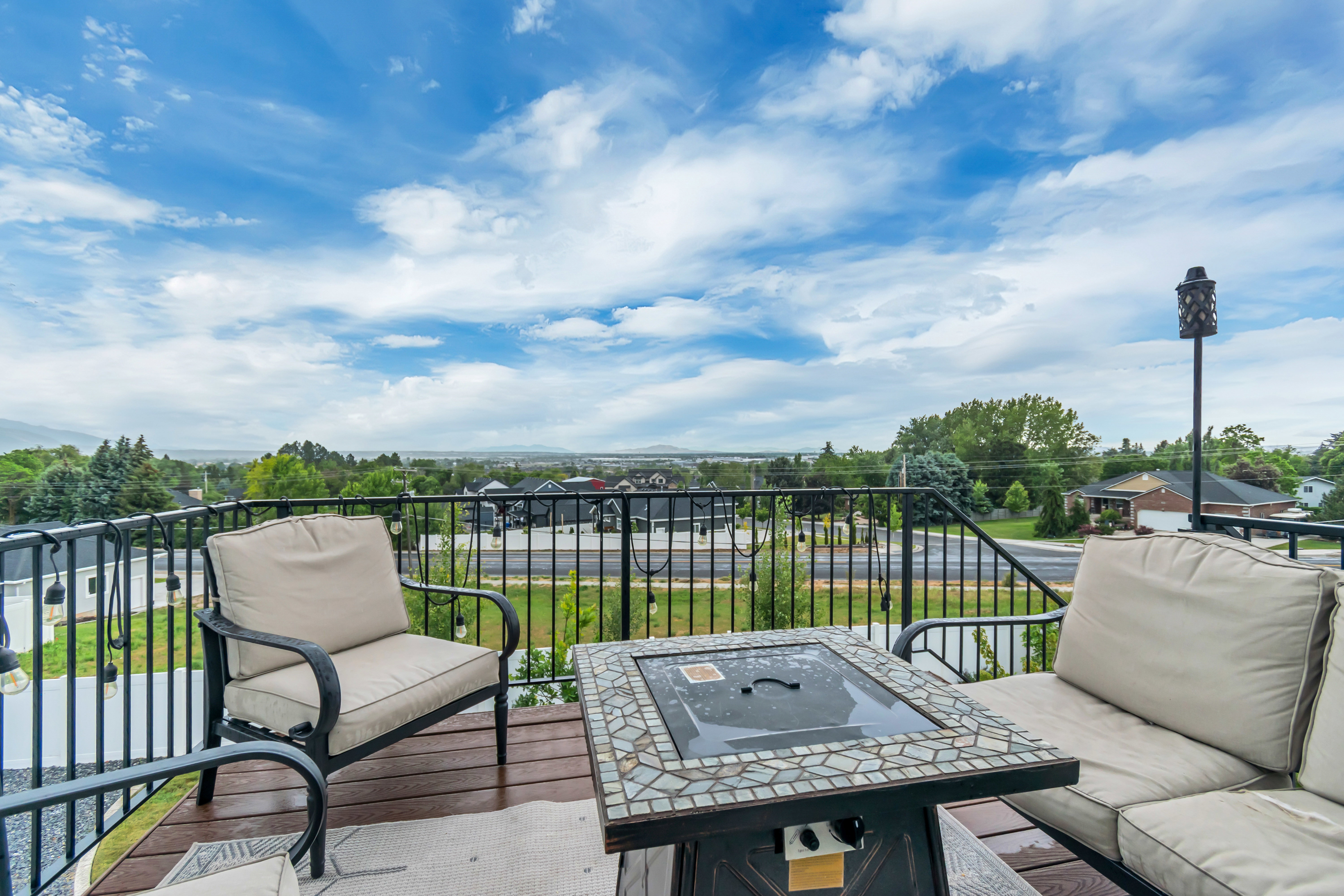 Spacious outdoor deck featuring wood-finish flooring, black metal railings, and a fire pit with a mosaic tile surround