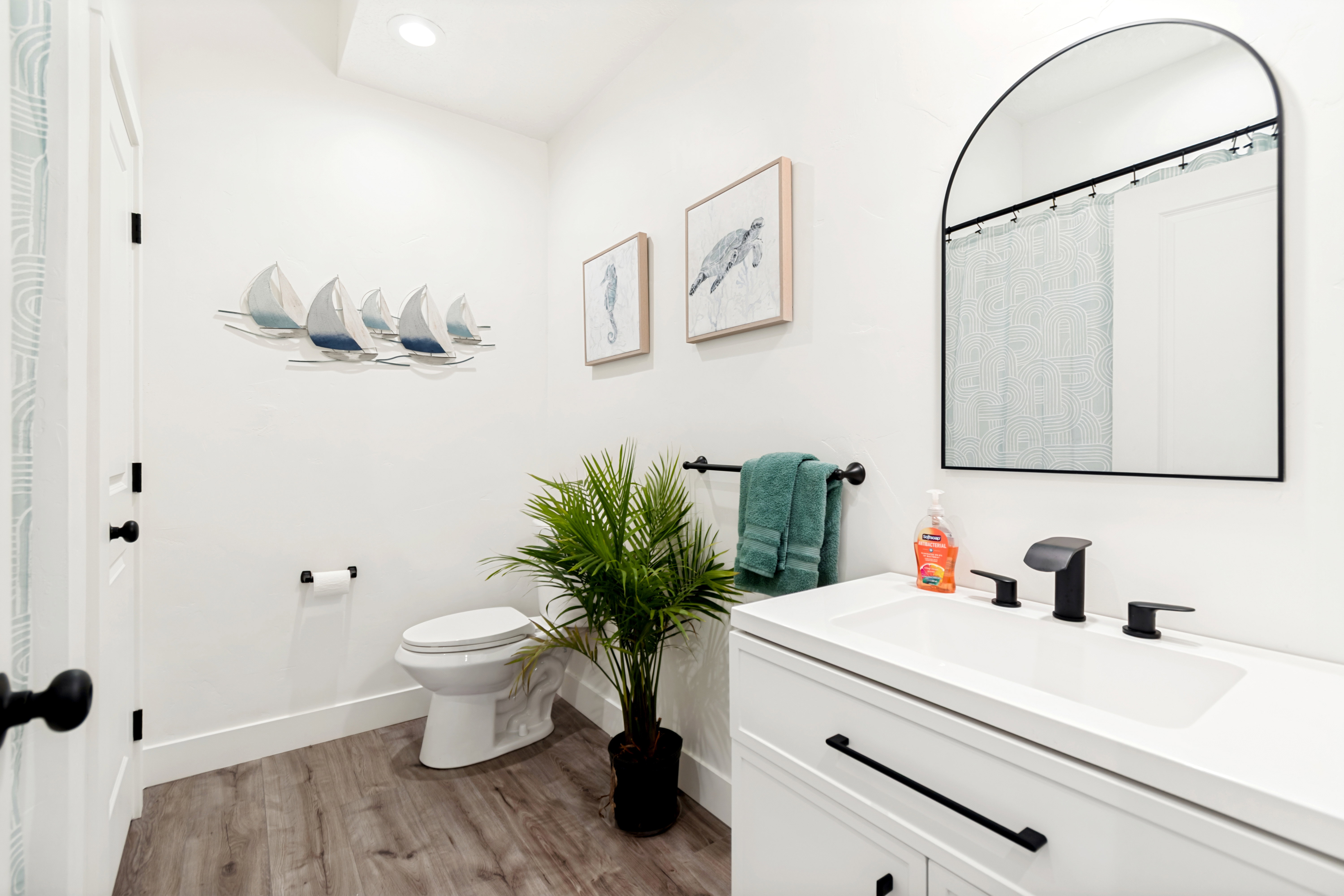 Modern bathroom featuring a white vanity with integrated sink, matte black hardware, arched mirror, and wood-finish flooring