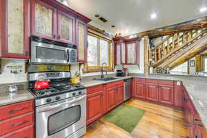 Kitchen featuring rustic red cabinetry with glass-front uppers, wood-finish flooring, and a stainless steel appliance suite including a range and microwave
