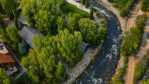 Riverside property featuring a pitched roof structure surrounded by mature trees, a natural stone riverbank, and a dirt path