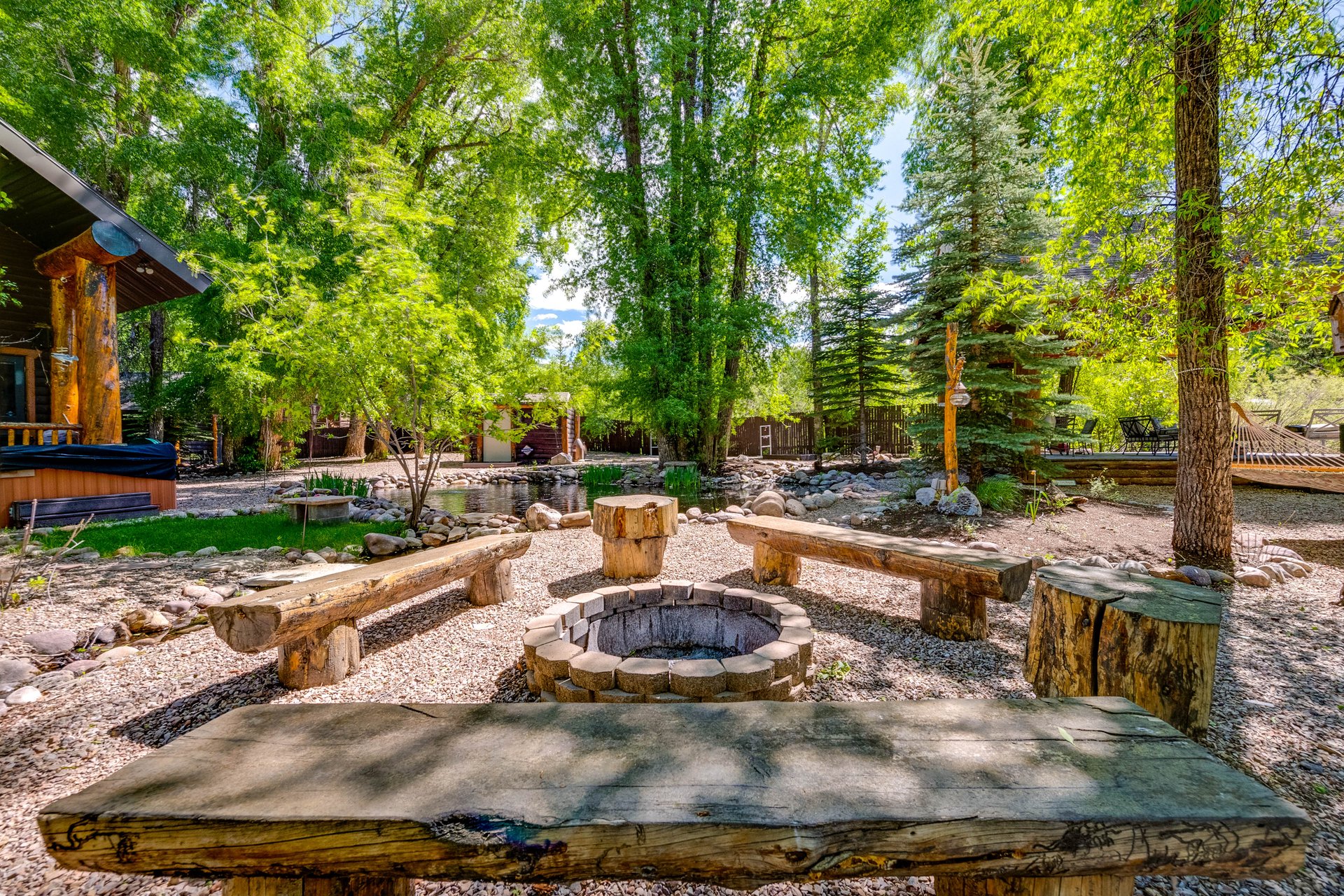 Outdoor entertainment area featuring a stone fire pit with surrounding log benches and stump seating