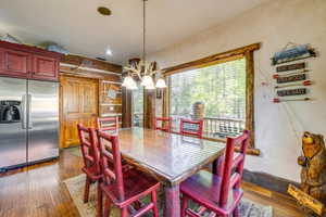 Dining area featuring a wood-finish table with a glass top, a large window, a rustic chandelier, wood-finish flooring, and a stainless steel refrigerator