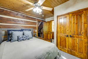 Wood-paneled ceiling with a ceiling fan, log walls, wood-paneled doors, and carpeted flooring