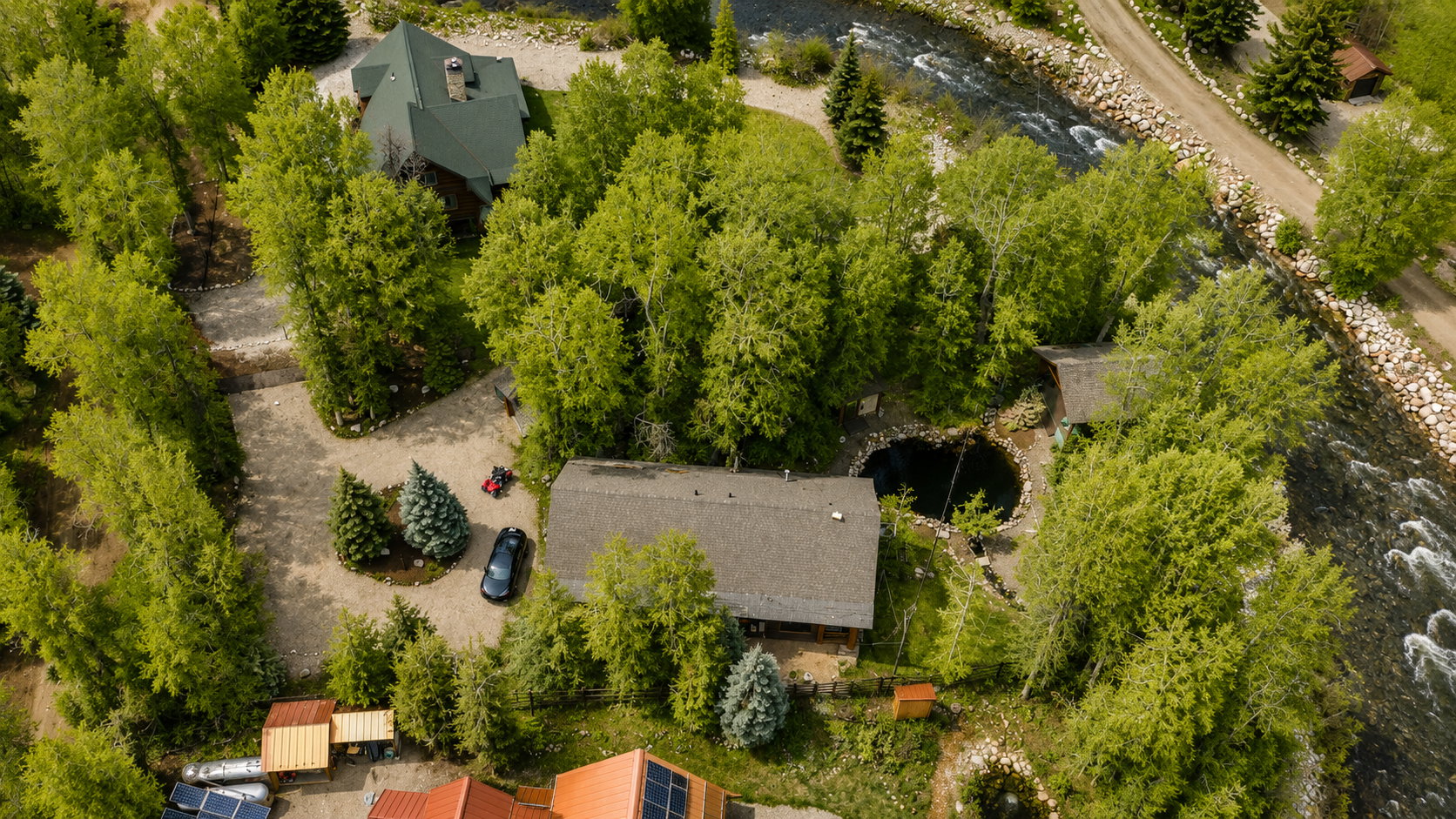 Riverside property featuring a main residence, an additional dwelling, mature trees, and a circular water feature