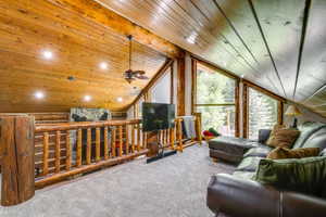 Loft area featuring sloped wood-paneled ceilings, exposed wood beams, and large picture windows