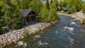Riverfront pavilion featuring exposed timber beams, a covered patio, and a stone-lined bank