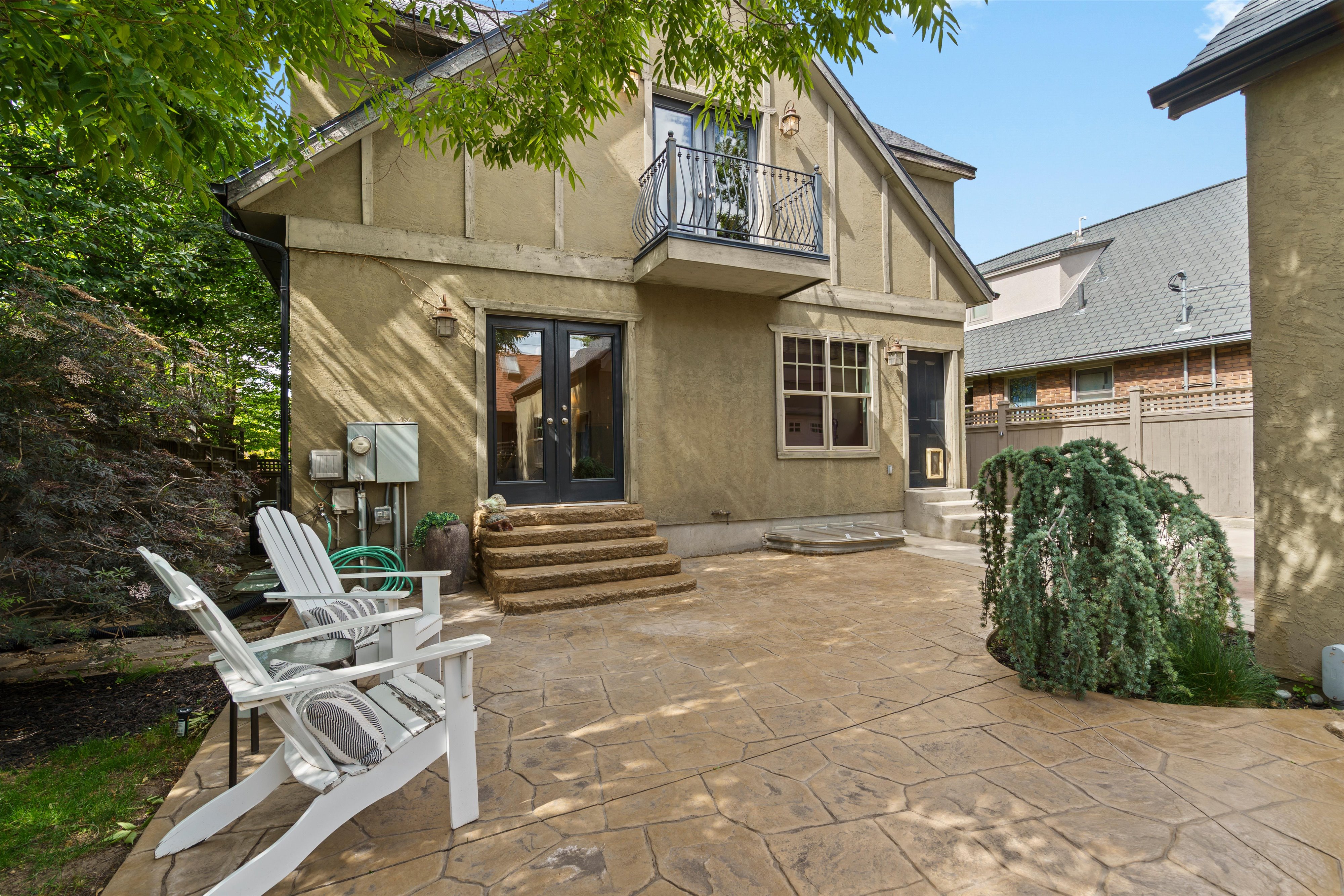 Stucco exterior featuring a second-story balcony with iron railing, stamped concrete patio, and mature landscaping