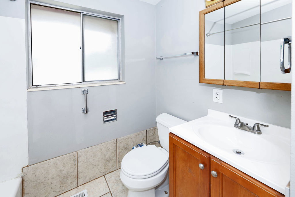 Bathroom featuring a wood-finish vanity with an integrated sink, a mirrored medicine cabinet, and a sliding window