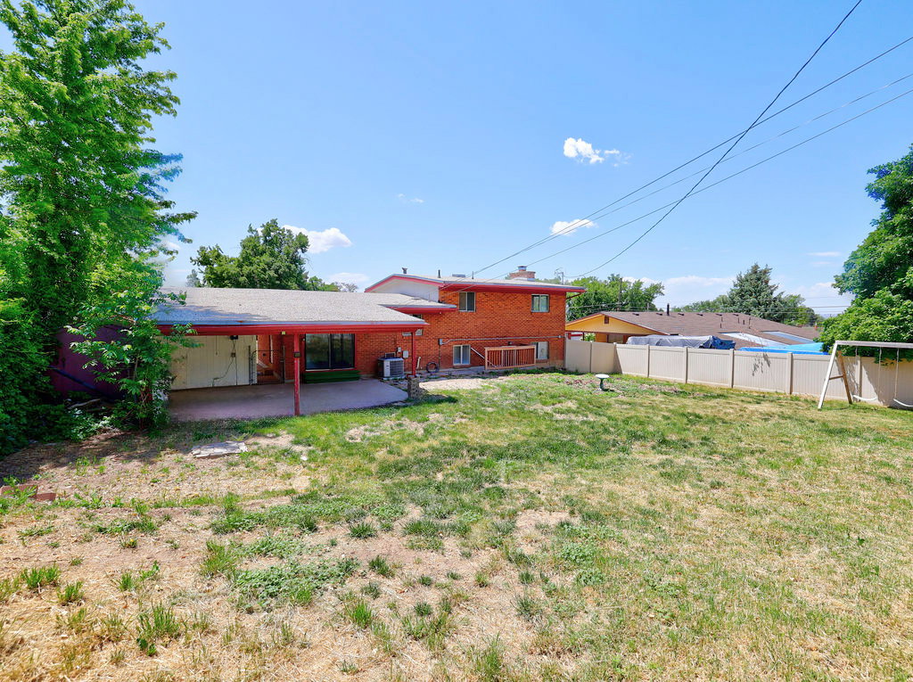 Expansive backyard featuring a covered patio with red support beams, a concrete slab, and an adjacent red brick exterior