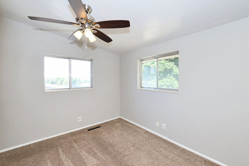 Carpeted room featuring two windows with natural light, a ceiling fan with integrated lighting, and light grey painted walls
