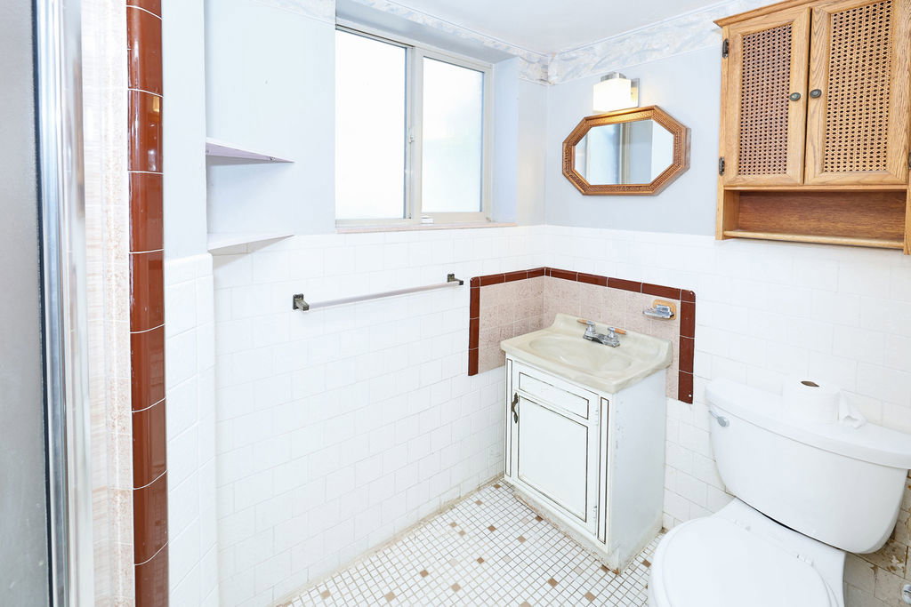 Bathroom featuring white wall tiling with an accent border, a white toilet, and a window for natural light