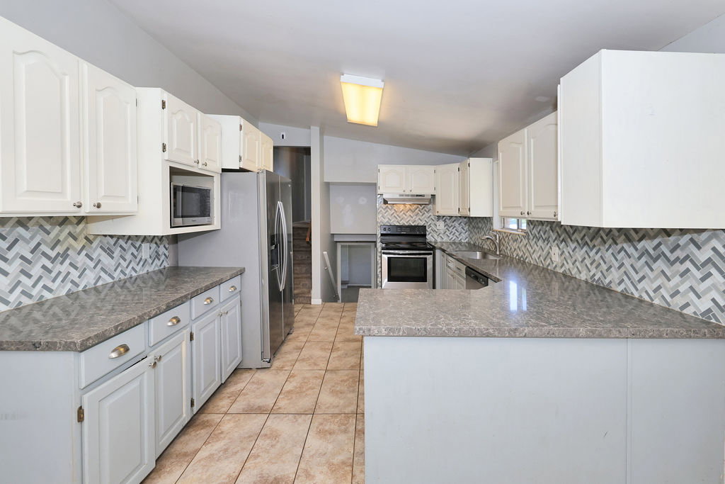 Kitchen featuring a breakfast bar, patterned tile backsplash, white upper cabinetry, light gray lower cabinetry, and stainless steel appliances