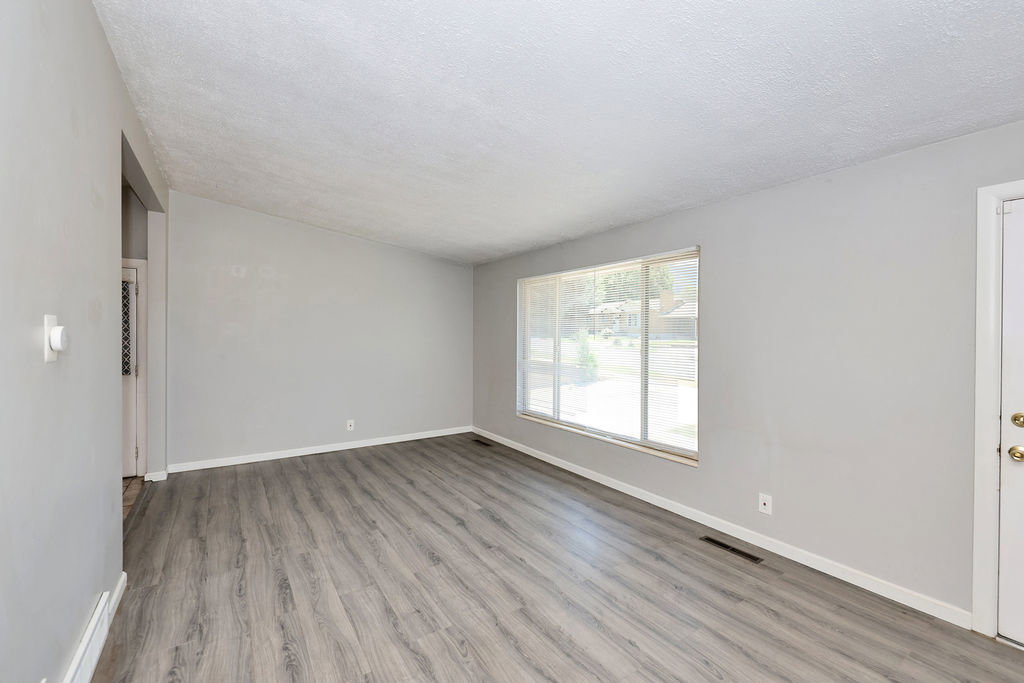 Spacious room featuring wood-finish flooring, light gray wall paint, and a large window with horizontal blinds
