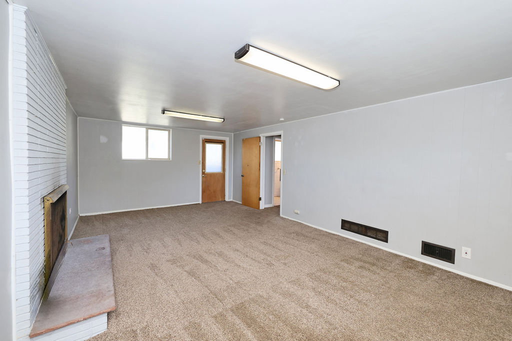 Carpeted room featuring a white brick fireplace with a stone hearth, two windows, and two natural wood doors