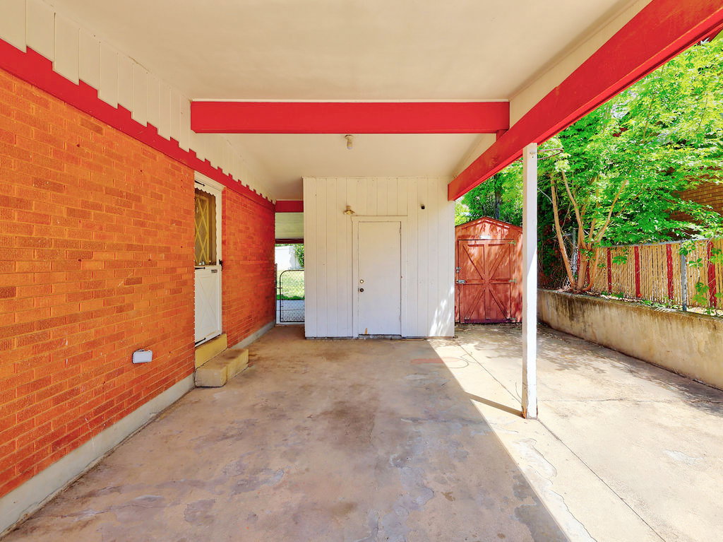 Covered concrete patio featuring a brick exterior wall, painted wood siding, red support beams, and an exterior storage shed