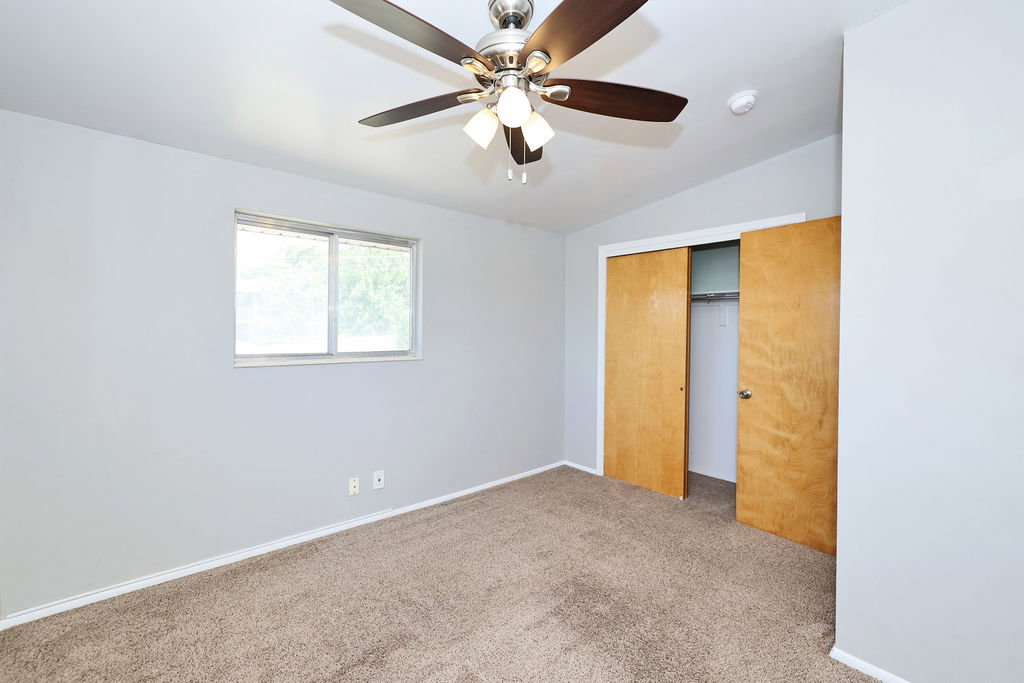 Bedroom featuring neutral-toned carpet, light gray walls, a window with natural light, and a ceiling fan with integrated lighting