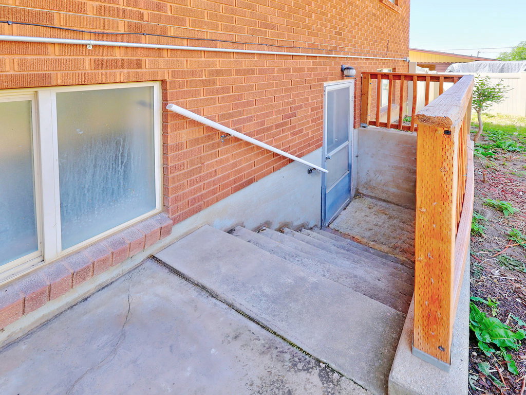 Concrete stairs descending to a basement entry, featuring a screen door and an overhead exterior light
