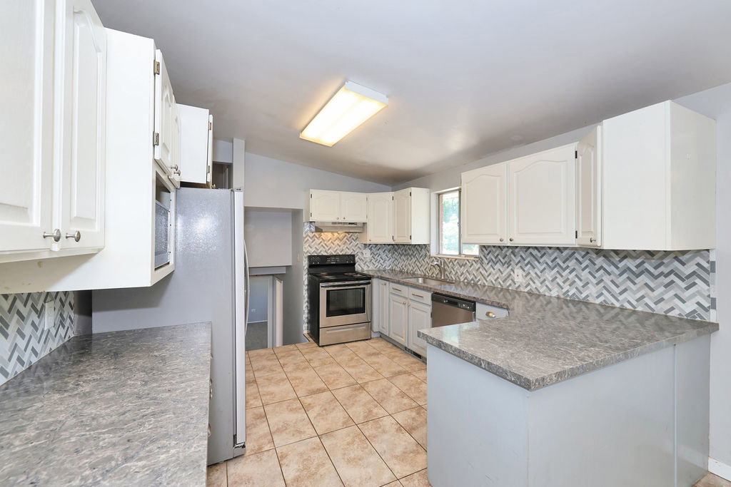 Kitchen featuring white cabinetry, gray countertops, stainless steel appliances, herringbone pattern tile backsplash, and tile flooring