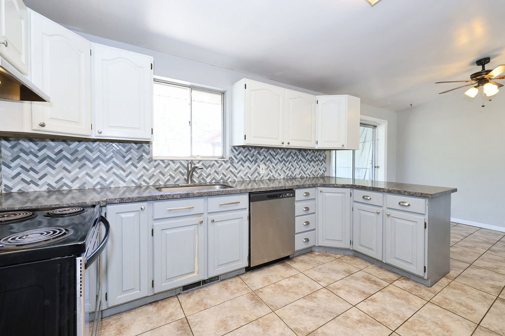 Kitchen featuring a patterned tile backsplash, light cabinetry, stone-finish countertops, stainless steel dishwasher, and tiled flooring