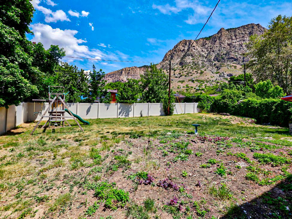 Expansive backyard featuring a partial privacy fence, mature perimeter greenery, and a prominent mountain backdrop