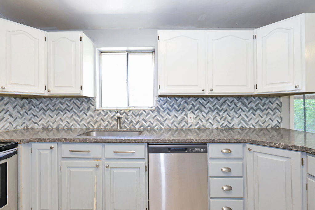 Kitchen with two-tone cabinetry, a herringbone tile backsplash, and a stainless steel sink