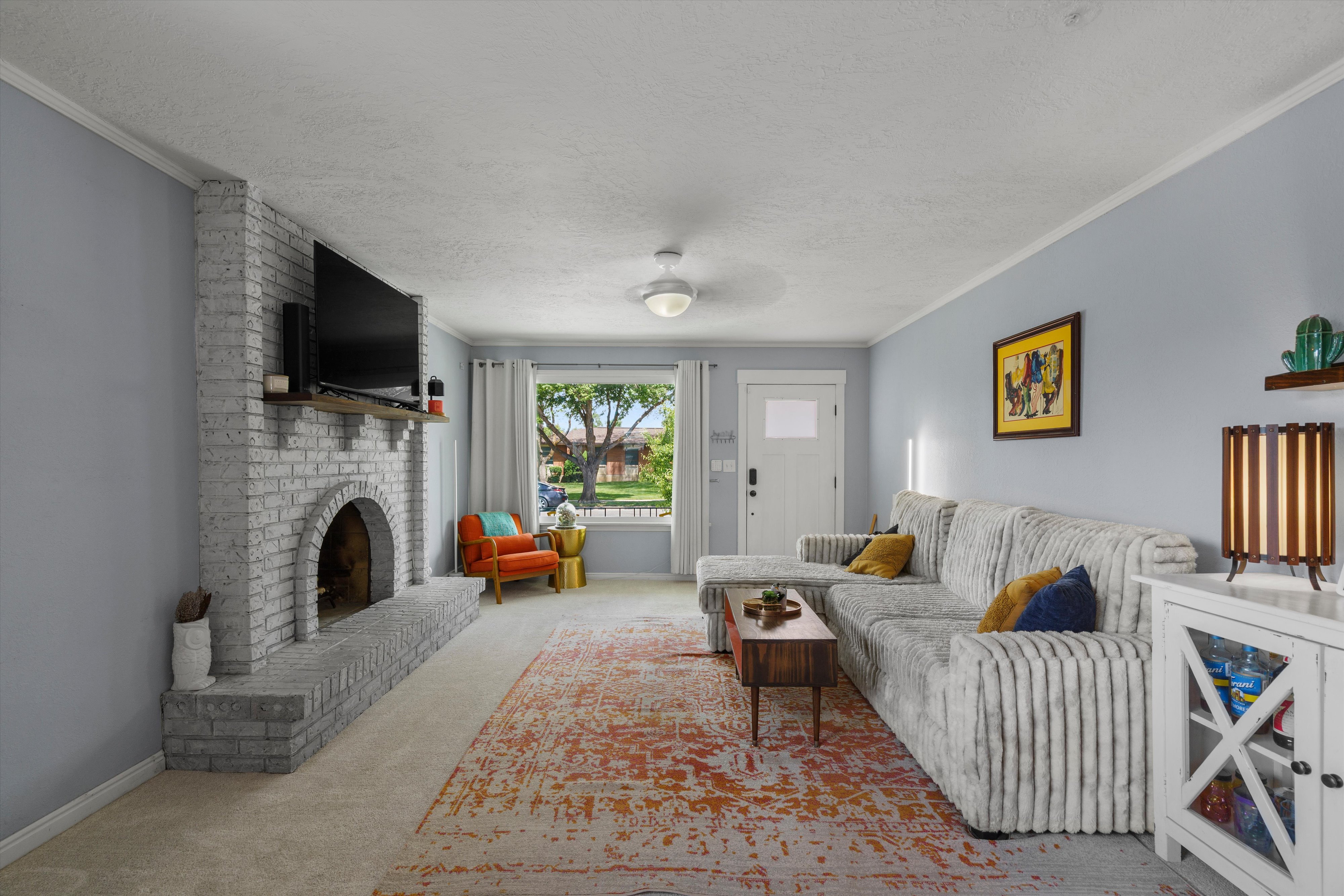 Living room featuring a painted brick fireplace with a wood mantle, neutral carpeting, and light blue wall tones