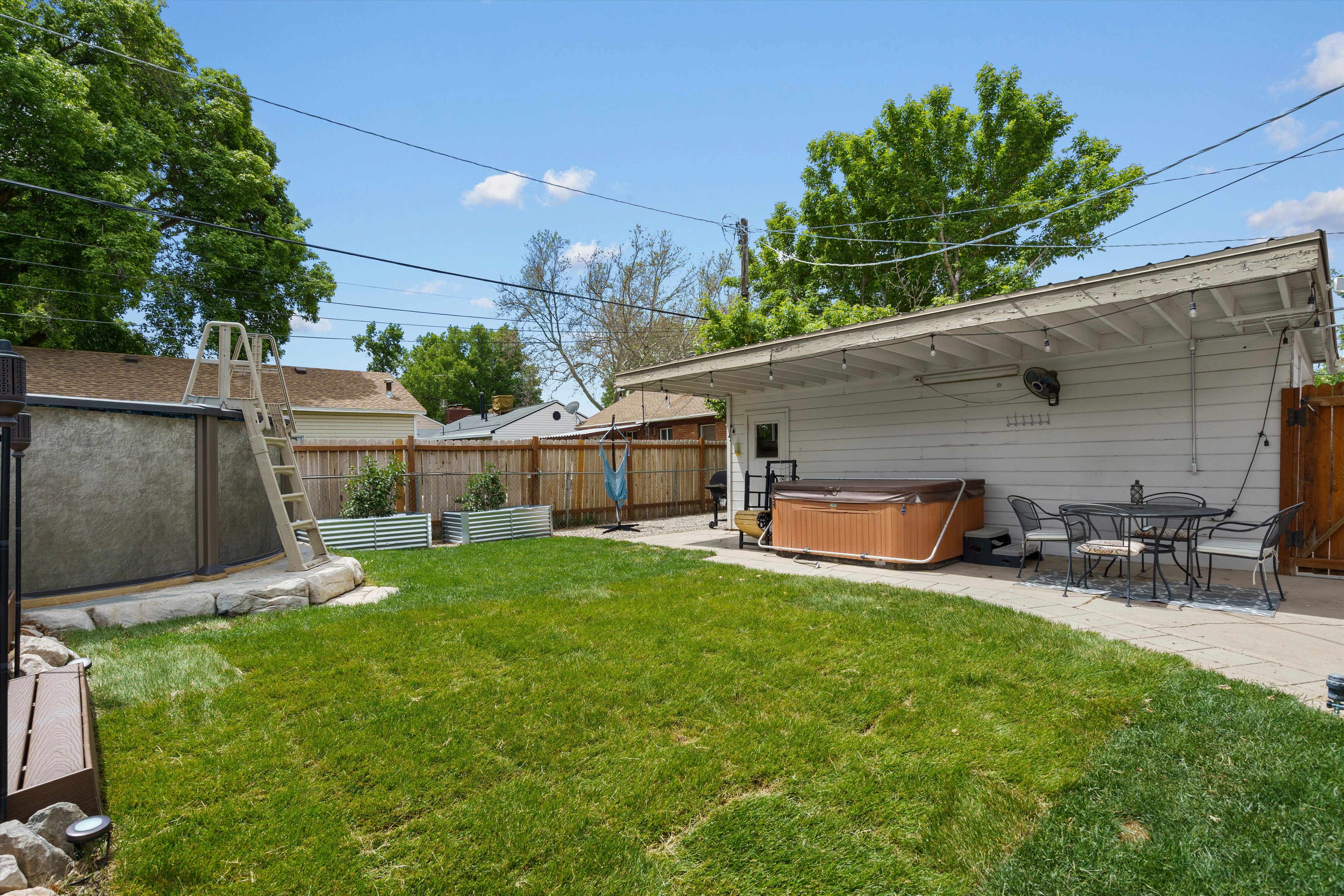 Expansive backyard featuring a lush lawn, an above-ground pool with a ladder, a concrete patio area, and a large spa